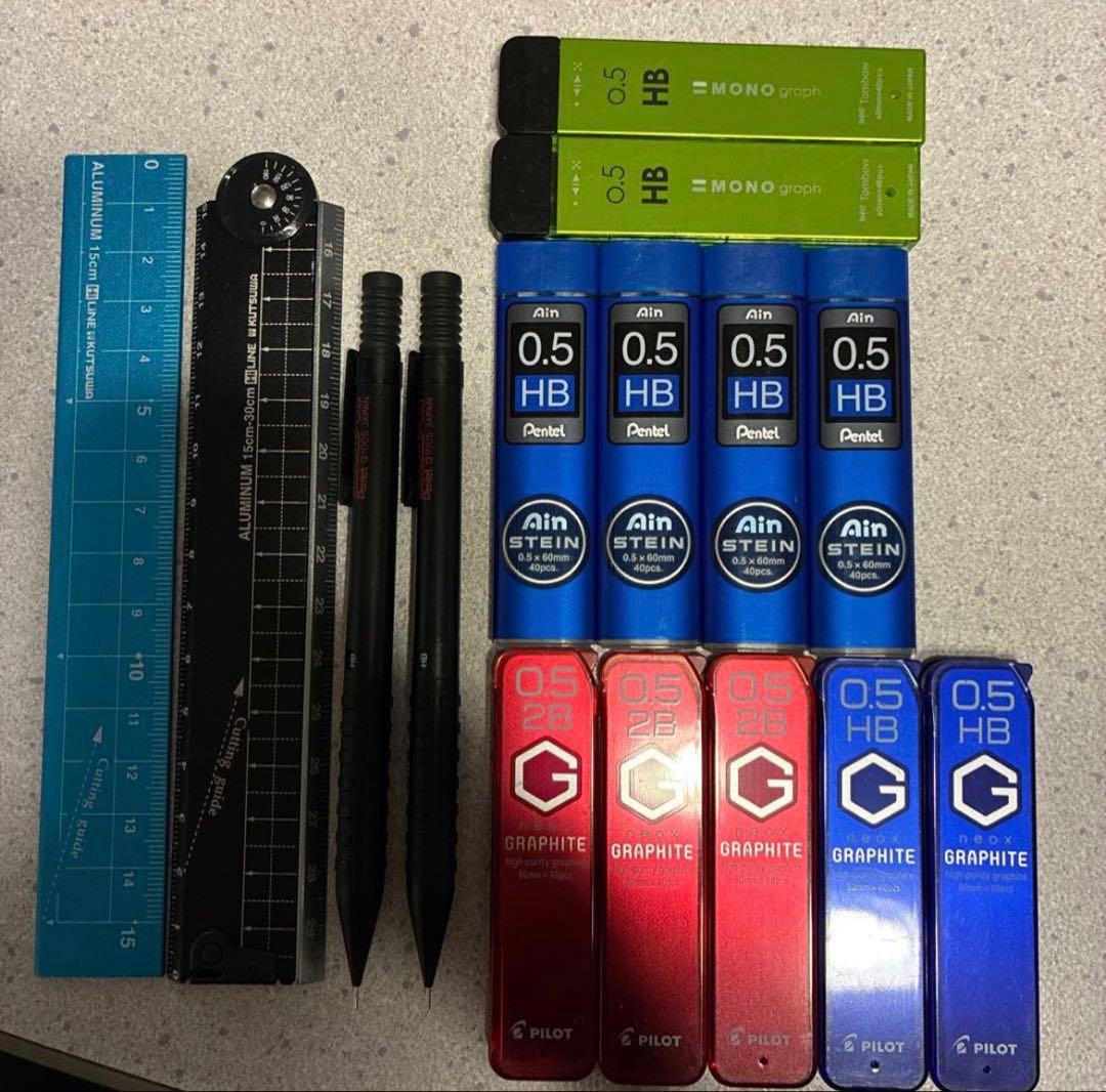 Photo showing multiple 0.5 mm mechanical pencil lead refill containers alongside two mechanical pencils and two rulers.