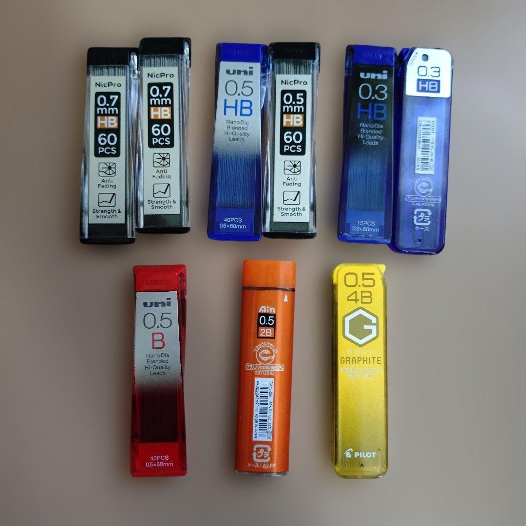 Several tubes of mechanical pencil lead refills (0.3, 0.5, 0.7 mm) from various brands arranged on a flat surface.