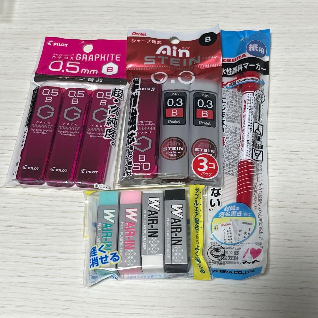 Photo of a stationery set showing multiple mechanical pencil refill packs, a red marker, and a small pack of erasers on a light wood surface.