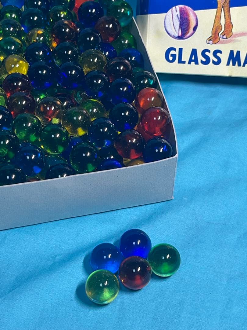 Colorful glass marbles in a white box with several marbles displayed on a blue cloth.