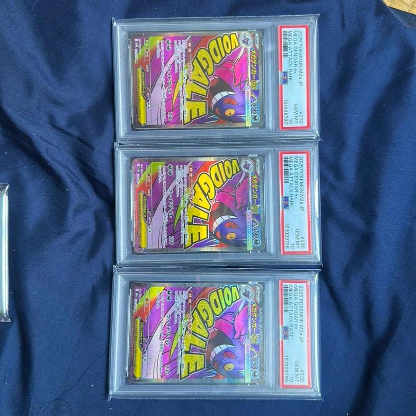Three PSA-graded Pokémon trading cards showing the Mega Gengar ex front artwork in slabs displayed on a blue cloth.