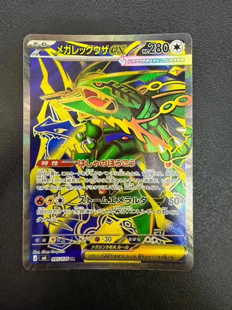 Front of a holographic Japanese Pokémon trading card (メガレックウザex) photographed on a dark surface.