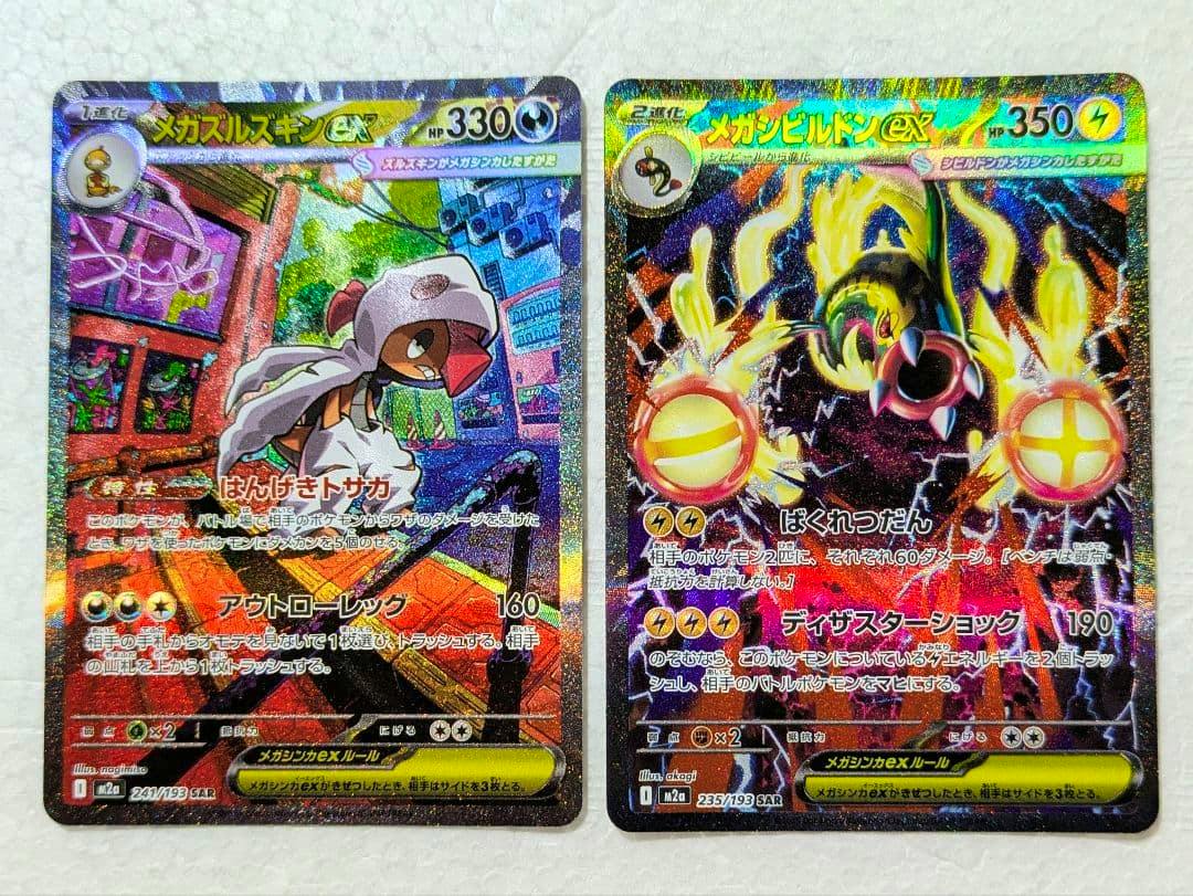 Two holographic trading cards (メガズルズキンex and メガシビルドンex) shown side by side on a white background.