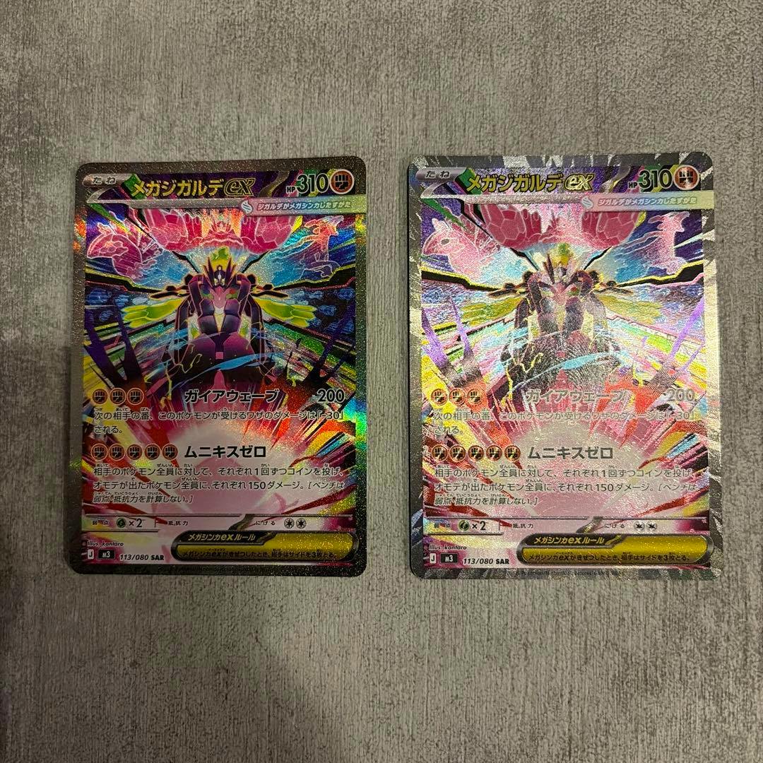 Front sides of two holographic Japanese trading cards from メガジガルデex SAR MEGA shown side by side on a gray surface.