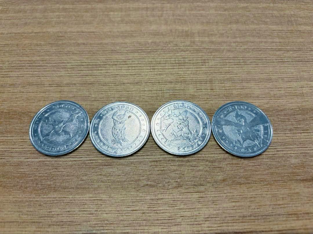 Four metal Pokémon battle coins showing character designs arranged in a row on a wooden surface.