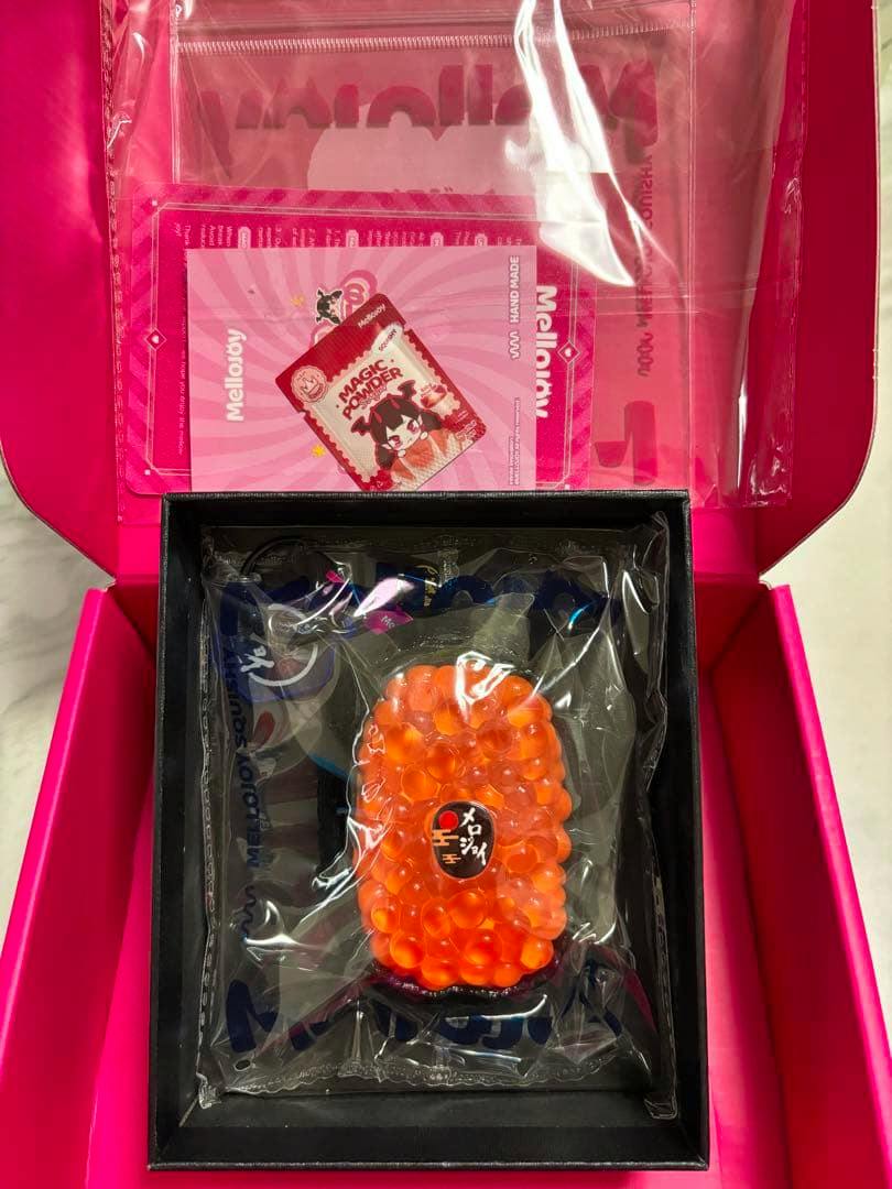 Top-down photo of the Mellojoy ikura (salmon roe) rubber squishy sealed in clear plastic inside a pink box with branded inserts.