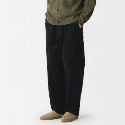 Front view of a model wearing black corduroy relaxed men's pants with hands in pockets.