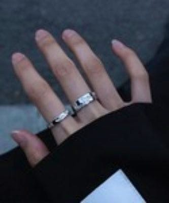 A hand wearing two men's rings on adjacent fingers.