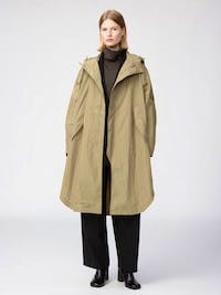 Front view of a model wearing a men's nylon hooded long coat in khaki over black clothing.