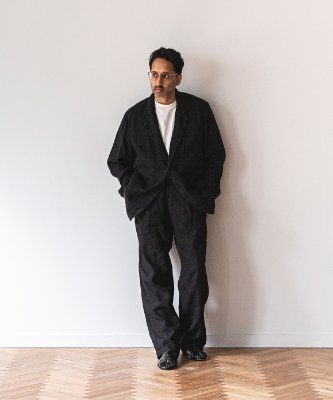 A man wearing the linen canvas jacket and matching trousers standing against a white wall.