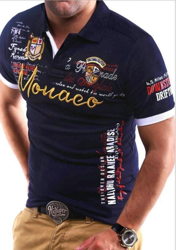 Man wearing a dark navy men's short-sleeve polo T-shirt with embroidered badges and a large "Monaco" script on the chest.