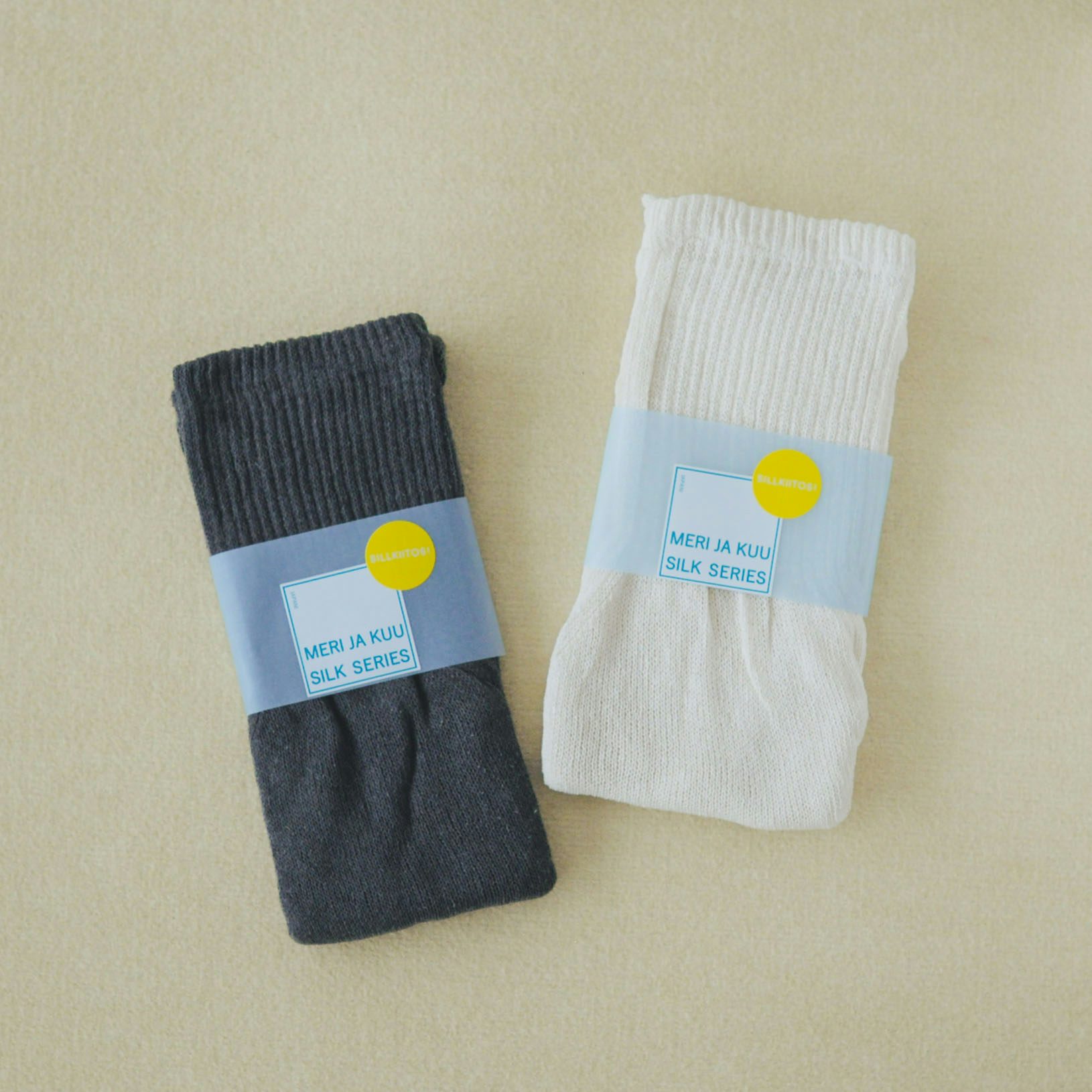 Two folded meri ja kuu silk inner pants (4分丈) in dark gray and off-white with paper labels on a pale background.