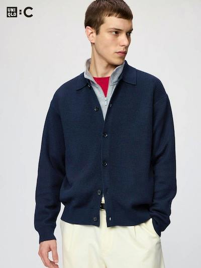 A male model wearing a navy shirt-collar cardigan buttoned over layered tops.