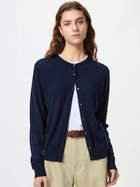 Front view of a navy merino crew-neck cardigan worn by a model over a white top and beige trousers.