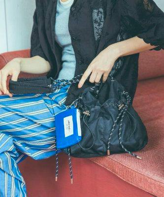 Seated model holding a black shoulder bag with a chain strap and an attached small blue pouch.