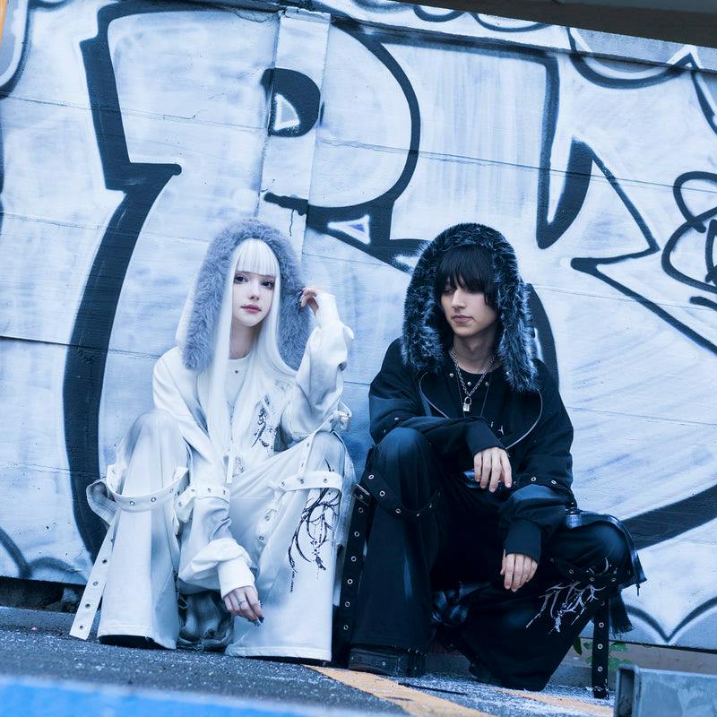 Two models wearing the Messenger ZIP Hoodie (one white, one black) with fur-lined hoods, seated against a graffiti-covered wall.