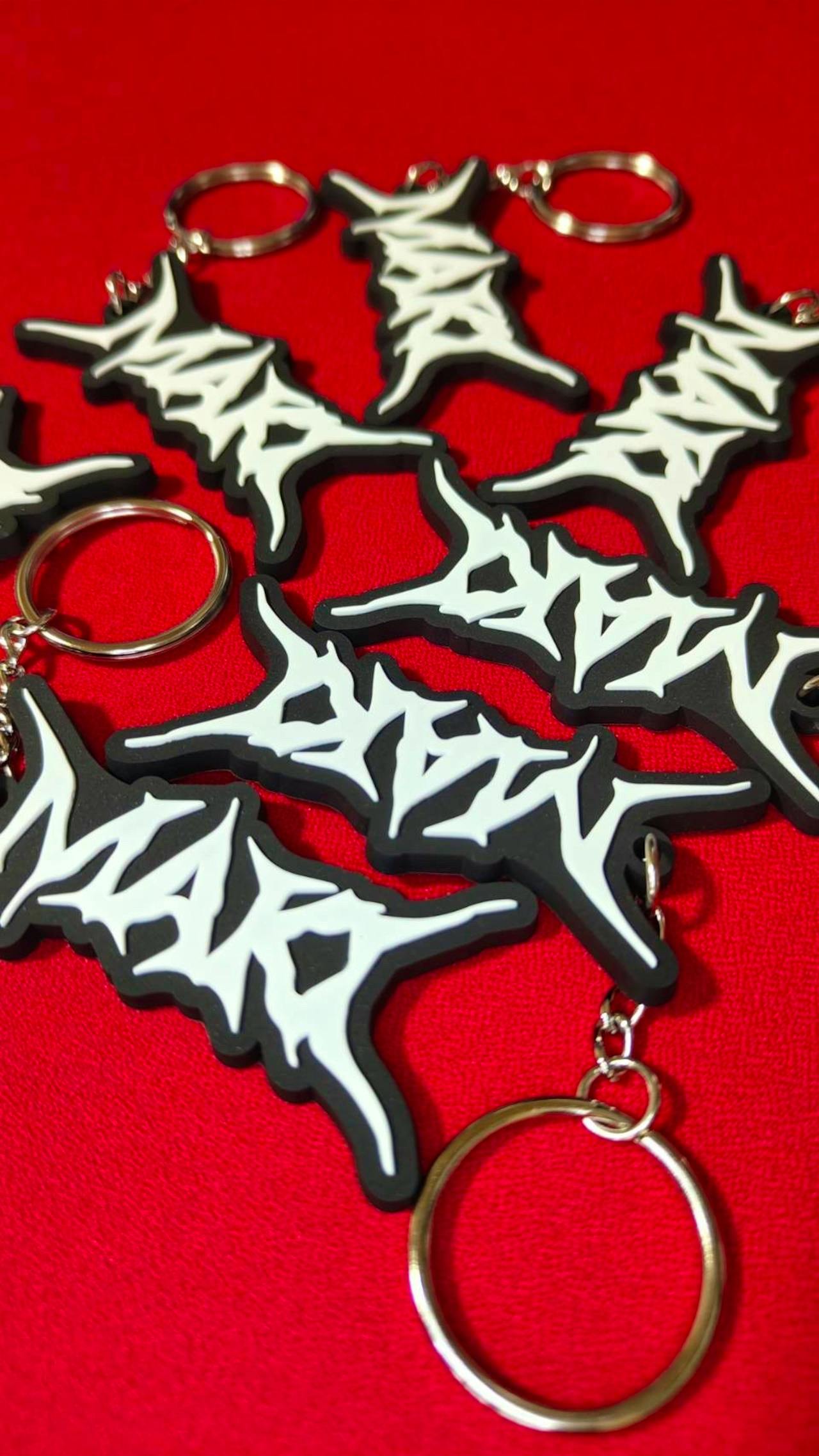 Multiple black rubber logo keychains with white stylized logos and metal key rings arranged on a red background.