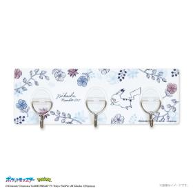 A three-hook metal wall bracket mounted on a floral patterned board with a small Pikachu illustration.