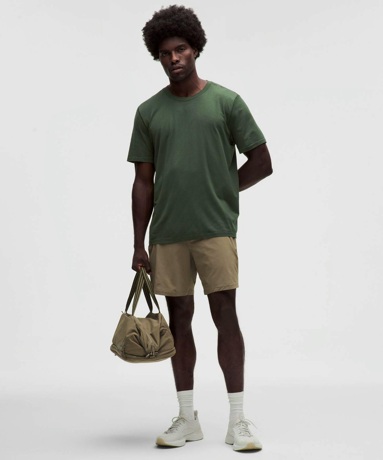 Male model wearing a green Metal Vent Tech relaxed-fit short-sleeve nylon shirt shown full-length while holding a bag.
