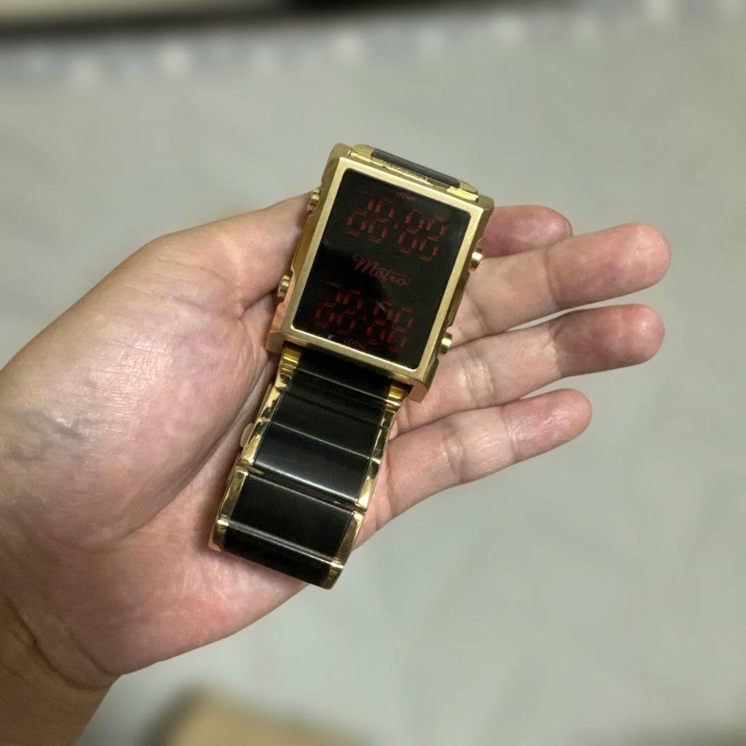 Gold Metro digital wristwatch with a rectangular black face and red LED display held in a hand.