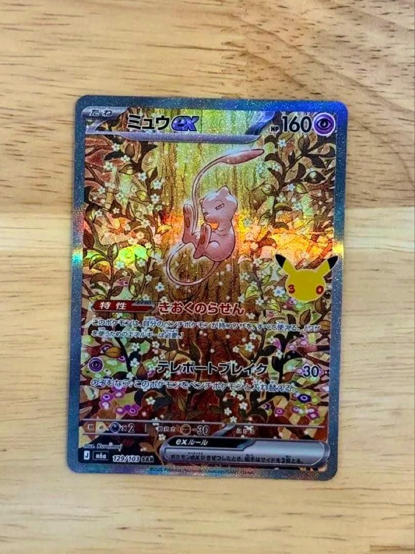 Front of the ミュウex 129/103 SAR trading card with holographic foil lying on a wooden surface.