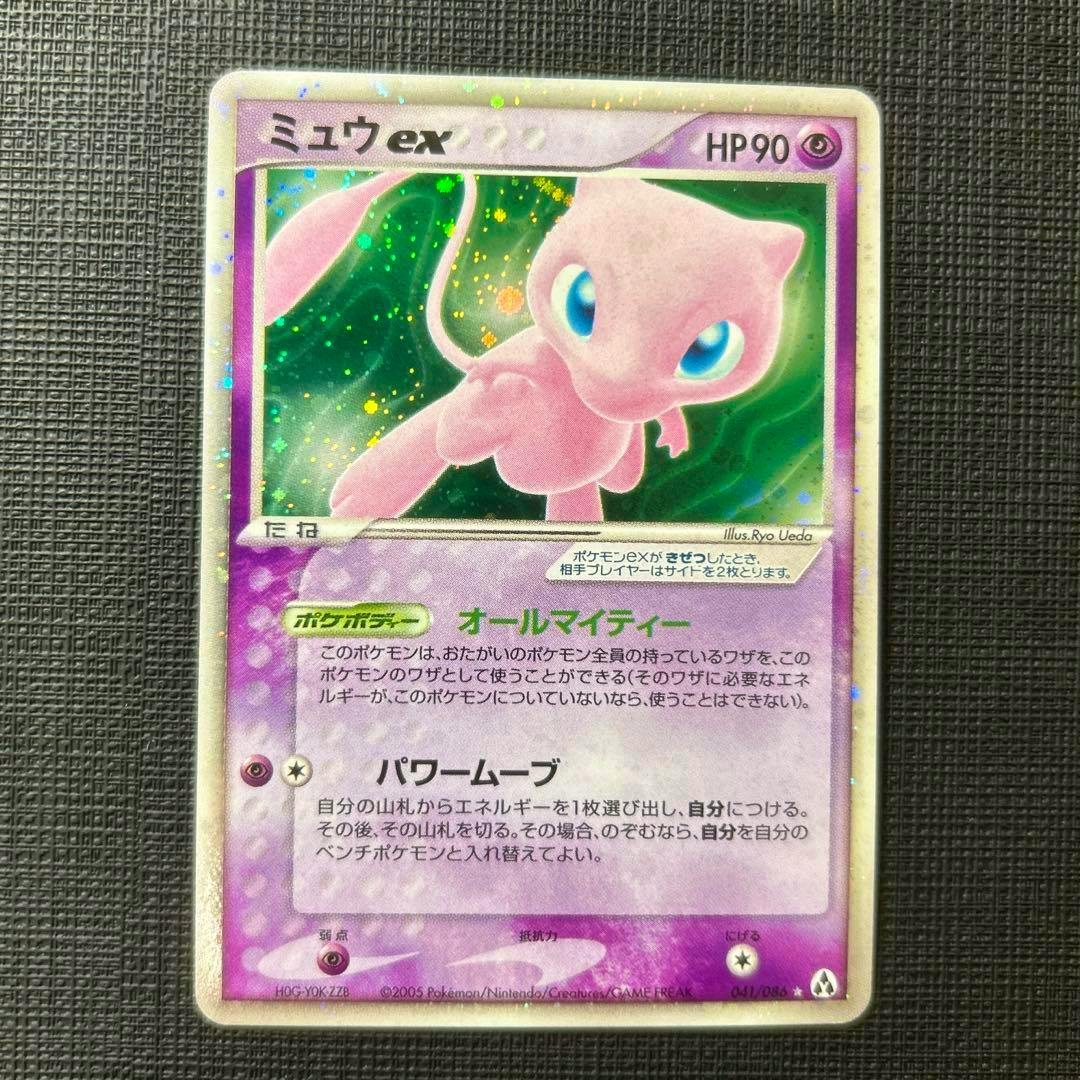 Full-front photograph of the ミュウex Japanese trading card showing Mew artwork and card text on a black textured background.