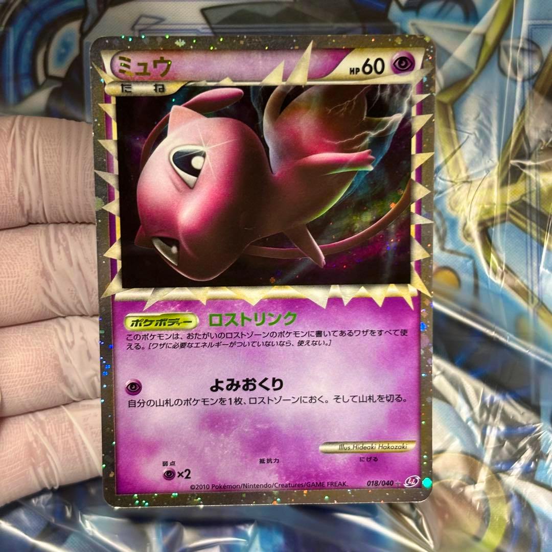 Full-view photo of the holographic Mew (ミュウ) trading card (018/040) held in a hand against a playmat background.