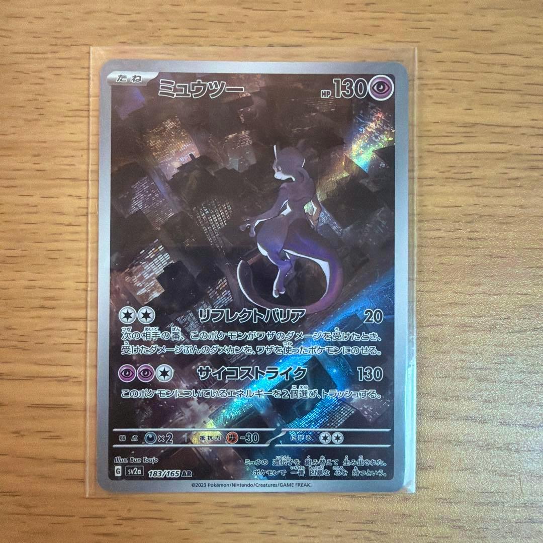 Front of a Mewtwo Pokémon trading card in a clear plastic sleeve on a wooden surface.