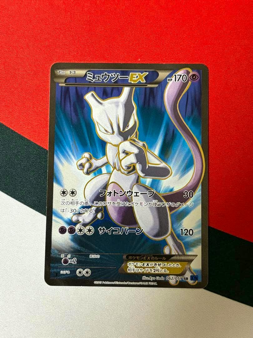 Photograph of the ミュウツーEX SR trading card showing Mewtwo artwork and Japanese text on a red, green, and white fabric background.