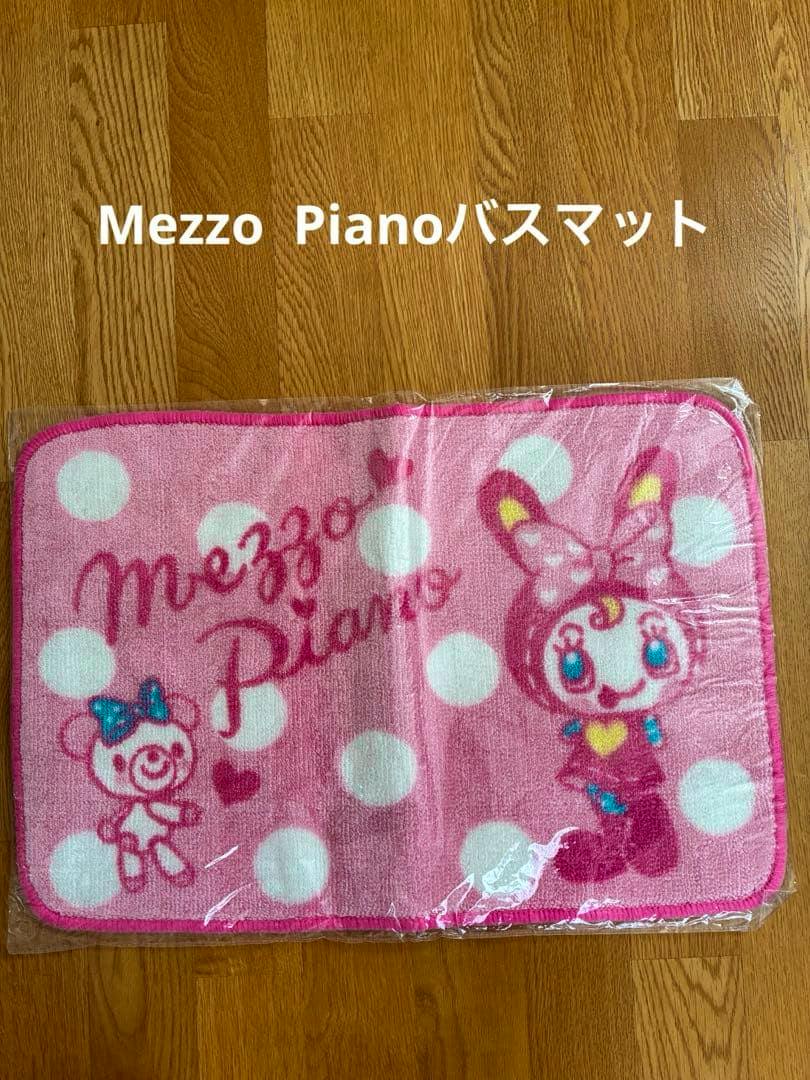 Pink Mezzo Piano bath mat with white polka dots and two cartoon characters on a wooden floor.
