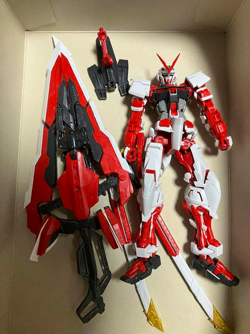 MG 1/100 Gundam Astray Red Frame Kai model parts and weapons (torso, limbs, shield, and swords) laid inside a box.