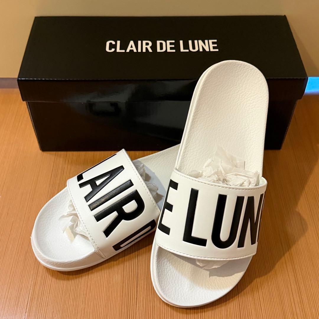 White rubber slide sandals with black "CLAIR DE LUNE" lettering on the straps displayed with the product box.