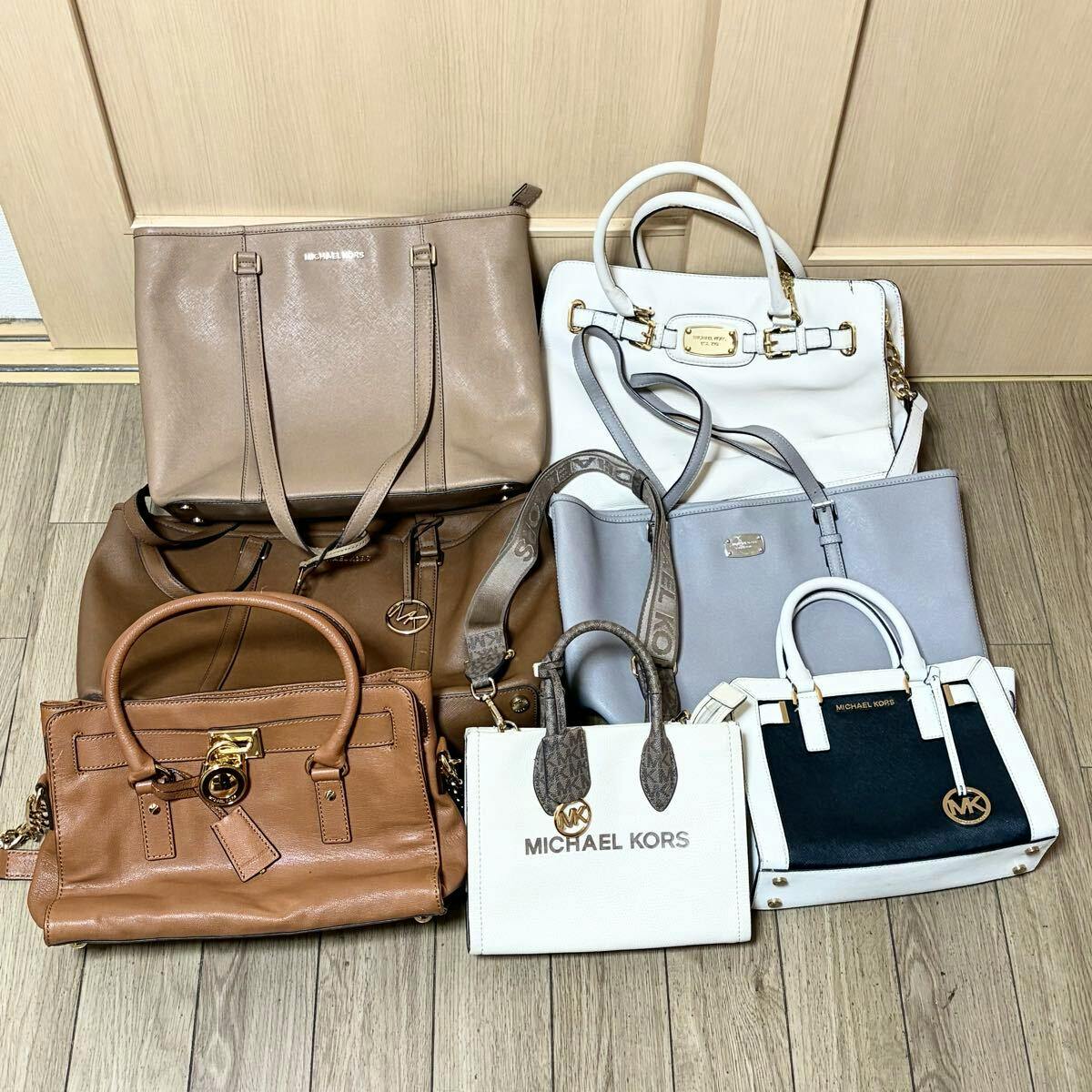 Several Michael Kors handbags and totes arranged on a wooden floor in front of a door.