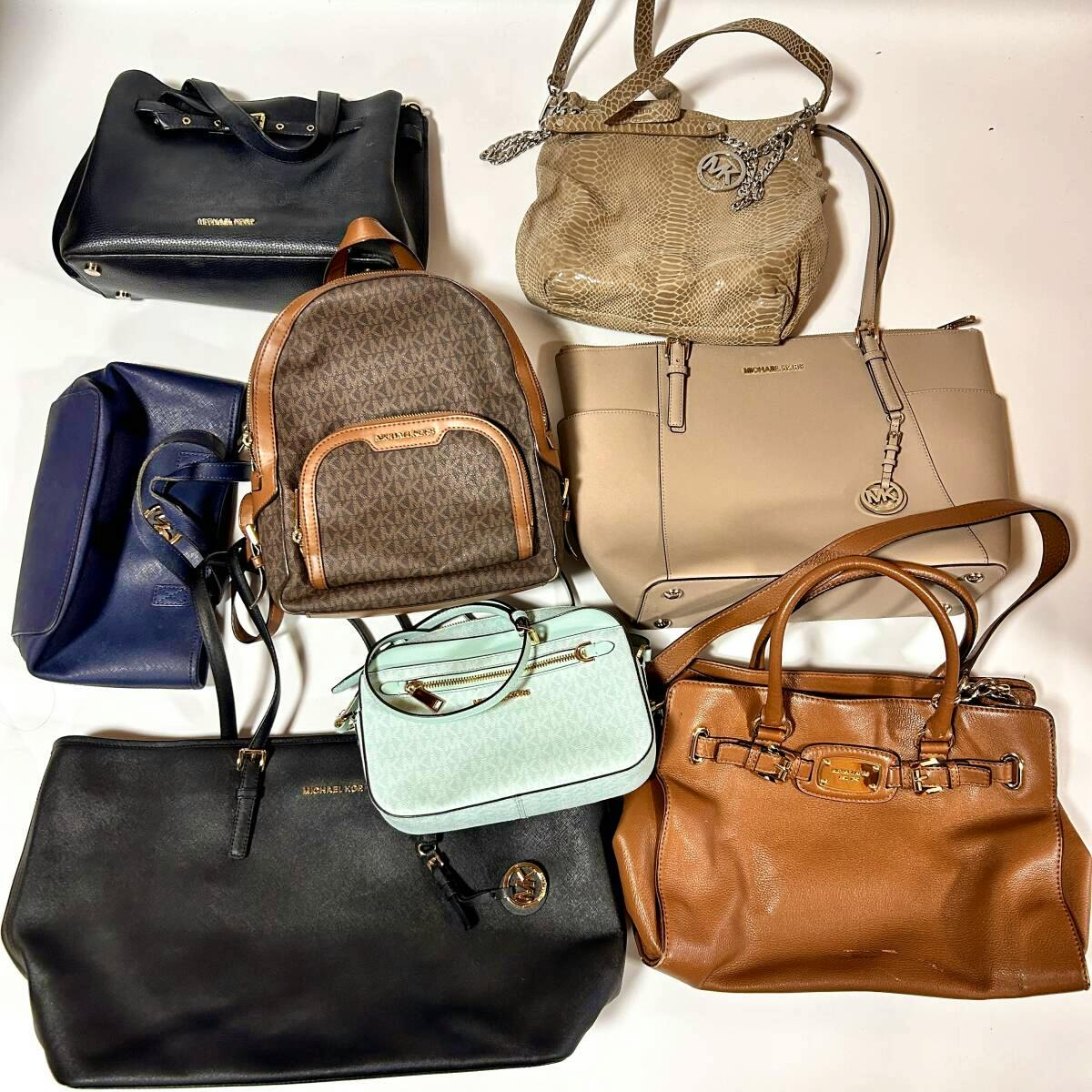 Eight Michael Kors bags and a backpack arranged together on a white background, showing different styles and colors.