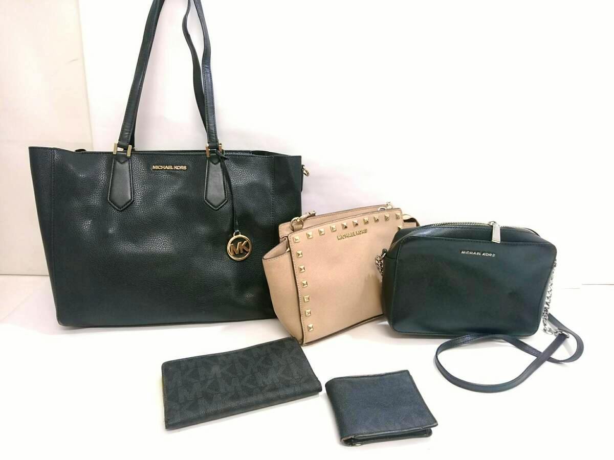 Five MICHAEL KORS items — a large black tote, a beige studded bag, a black crossbody, and two wallets — arranged on a white background.