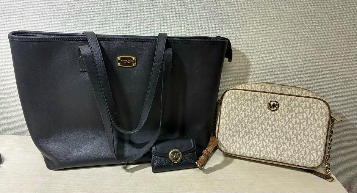 A black Michael Kors tote bag, a beige MK monogram crossbody bag, and a black Michael Kors key case displayed side by side.