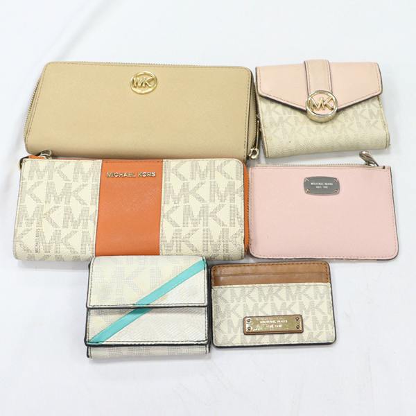 Six Michael Kors wallets and cardholders arranged on a white surface, showing MK monogram patterns and various colors.