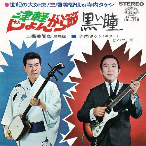 Front cover of the 7" vinyl record showing two men holding instruments (one traditional three-string instrument and one electric guitar) with Japanese text.