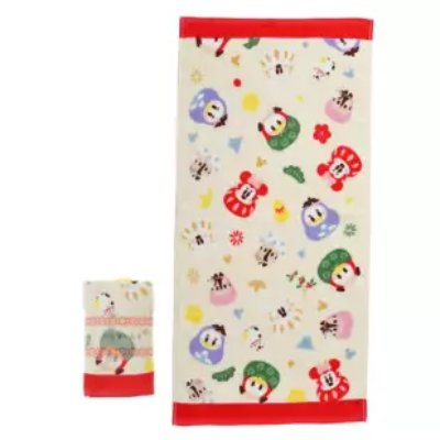 A face towel with red top and bottom borders and colorful Daruma-style Mickey and friends pattern, with a rolled towel beside it.