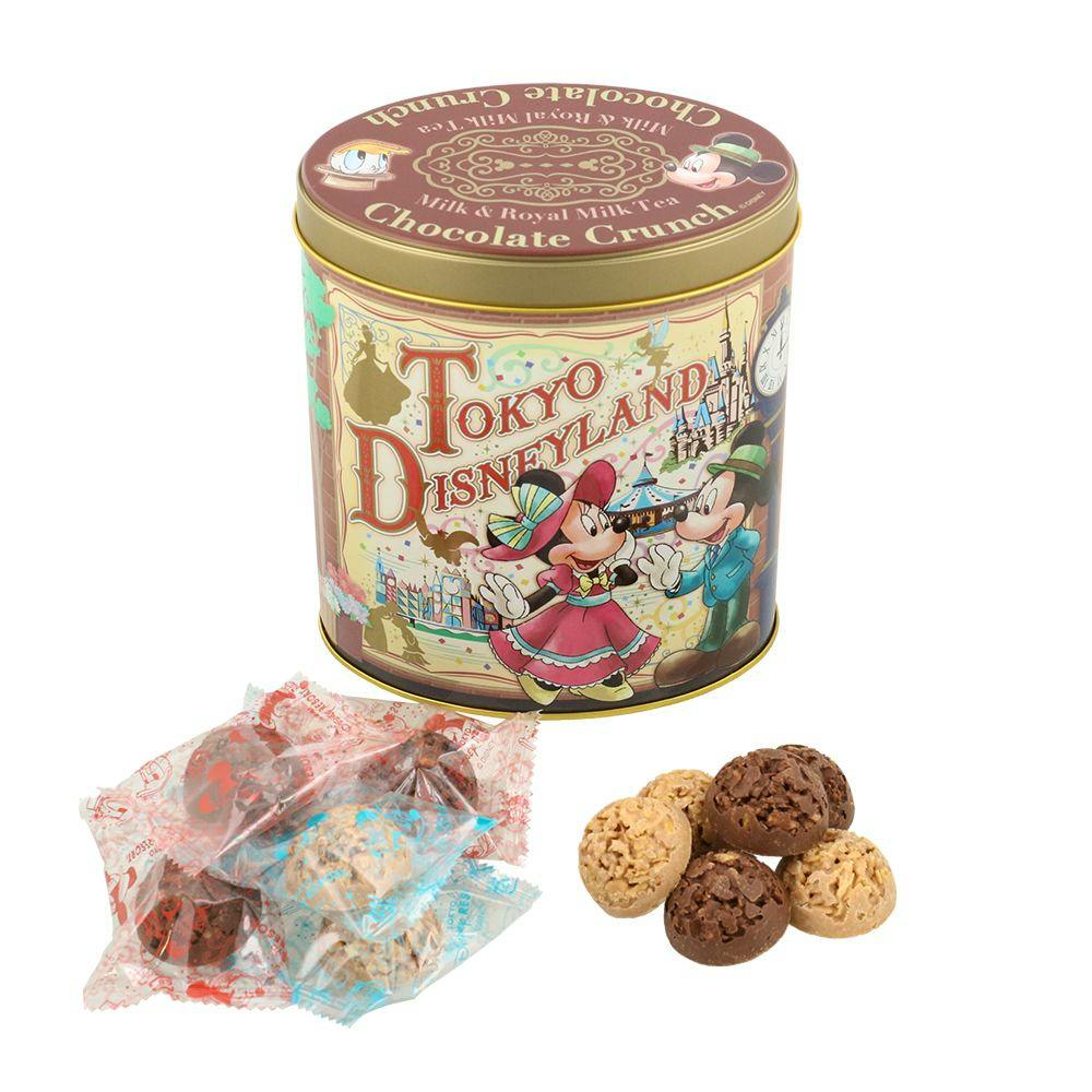 A decorated Tokyo Disneyland tin of chocolate crunch shown with several wrapped and unwrapped bite-sized chocolate crunch pieces.