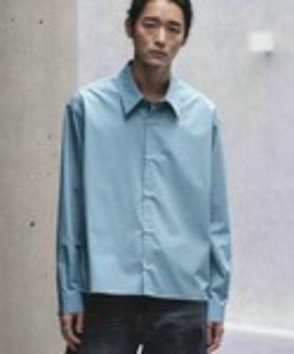 Male model wearing a light blue micro span cropped men's shirt with long sleeves against a concrete wall.