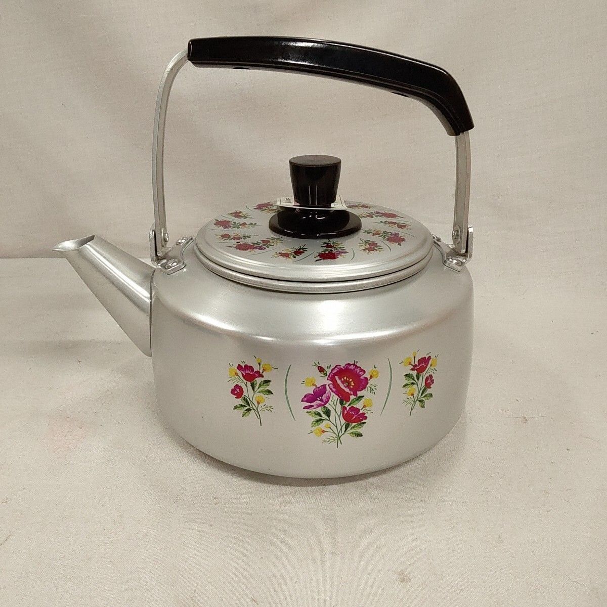Aluminum kettle with floral decals, a black handle and lid knob, photographed on a plain background.