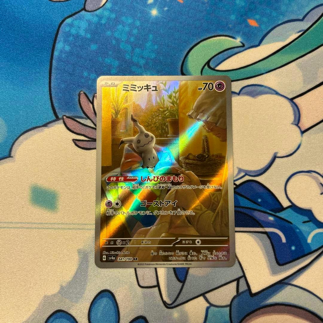 Holographic ミミッキュ Pokémon trading card shown face-up on a colorful playmat.