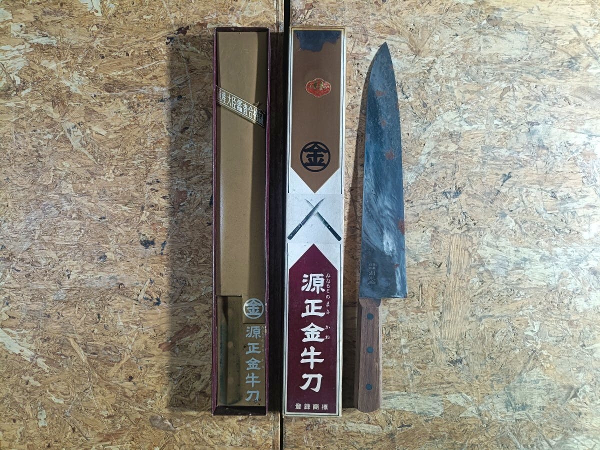 A chef knife with a wooden handle and its original box shown on a wooden surface.