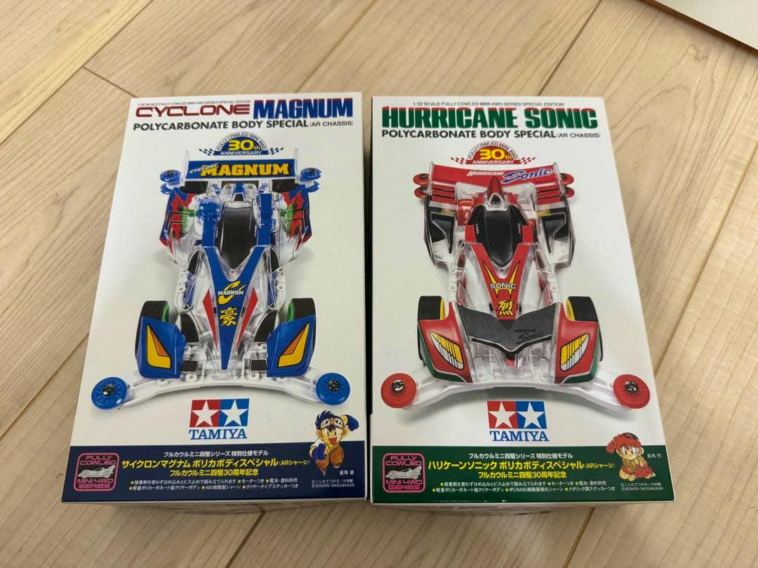 Two Tamiya polycarbonate body special model kit boxes showing Cyclone Magnum (left) and Hurricane Sonic (right) on a wooden floor.