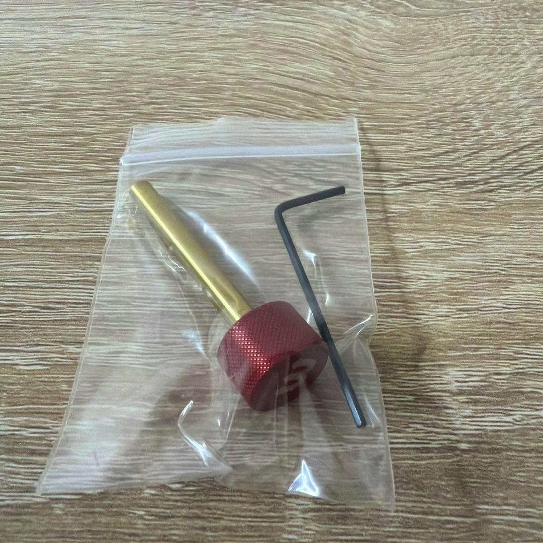 A gold shaft checker with a red knurled collar and a black L-shaped hex key inside a clear plastic bag on a wood surface.