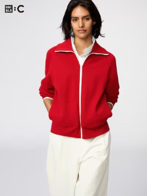Model wearing a red zip-front cardigan with white trim and white pants against a white background.