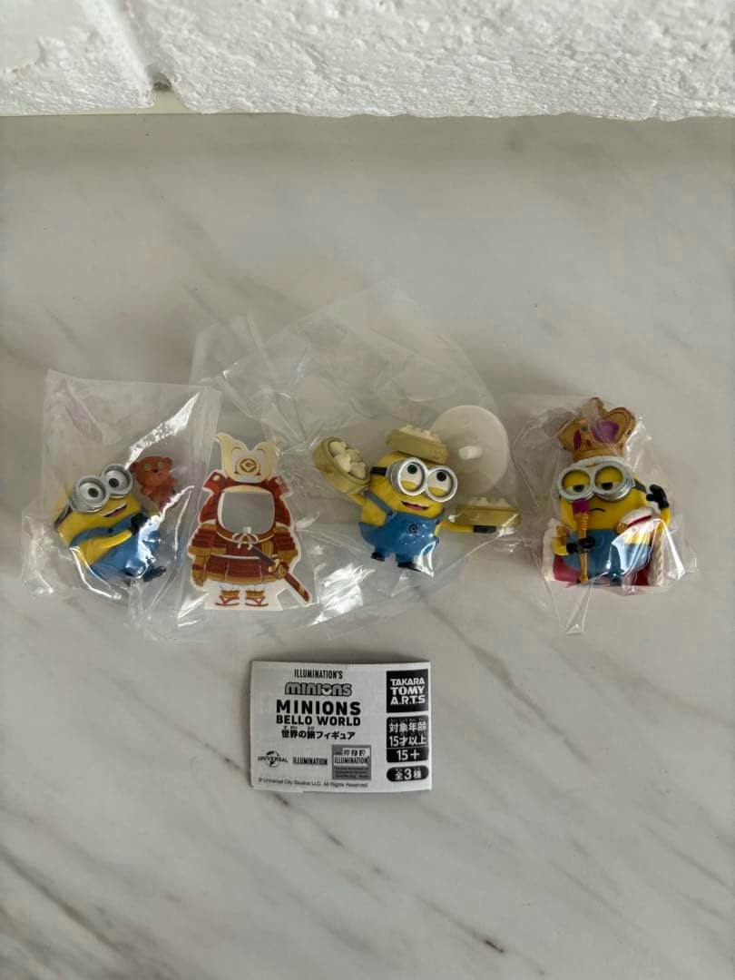 Photo of three Minions BELLO WORLD travel plastic figures in individual clear bags with the product paper insert visible.