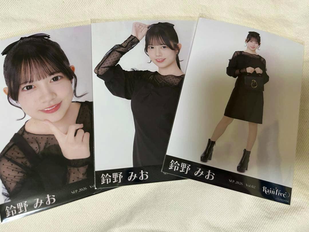 Three printed photographs of 鈴野みお wearing a black outfit arranged on a light fabric background.