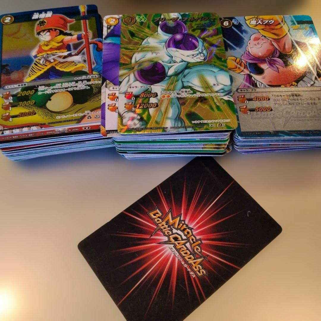 Stacks of Miracle Battle Carddass Dragon Ball trading cards with one card showing the card-back logo in the foreground.